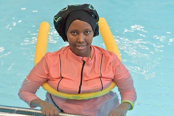 Kvinna står i en pool och håller i bassängkanten med en badnudel runt överkroppen.